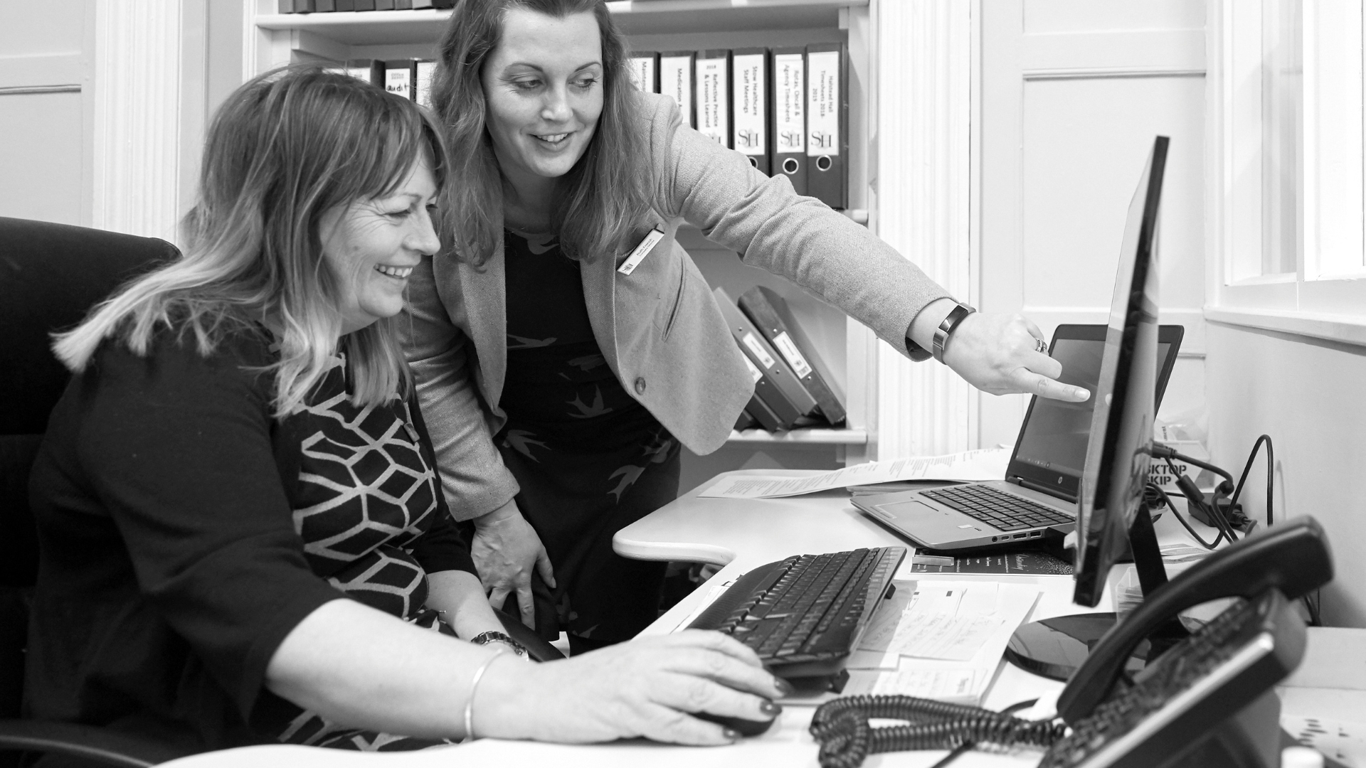 two woman looking at a computer, one pointing and smiling