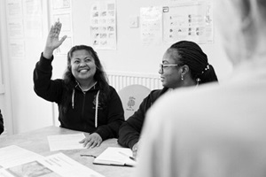 Two women sat at a table, one has her hand in the air